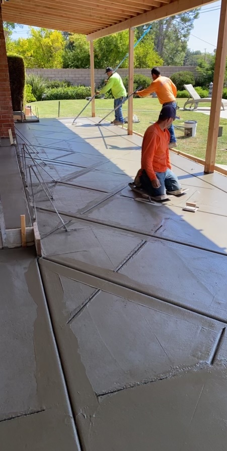 Image 2: A paito of still wet concrete with a hash texture in it.  There are 3 men smoothing out and creating the texture.